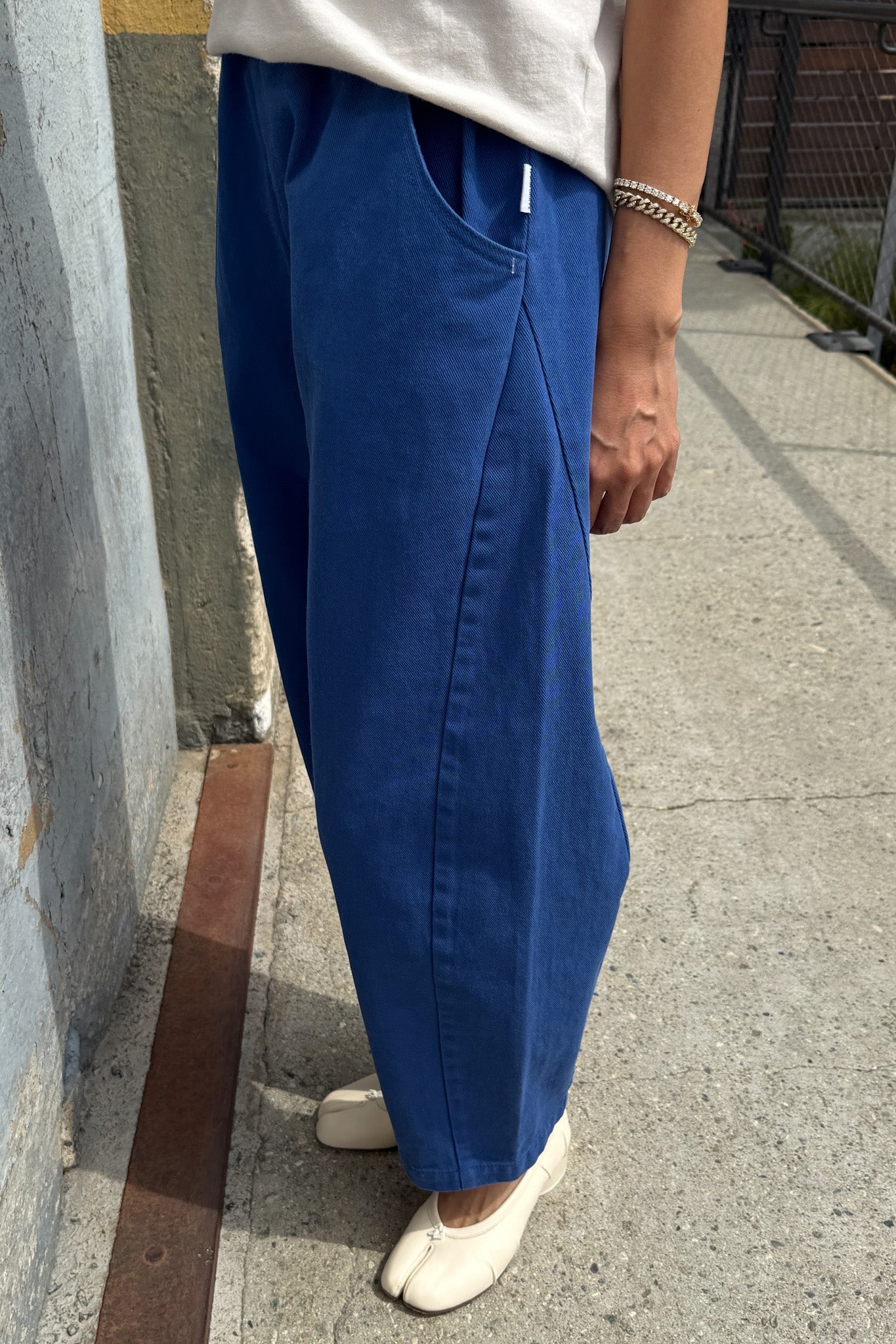 Person wearing blue pants and a white shirt standing on a sidewalk.