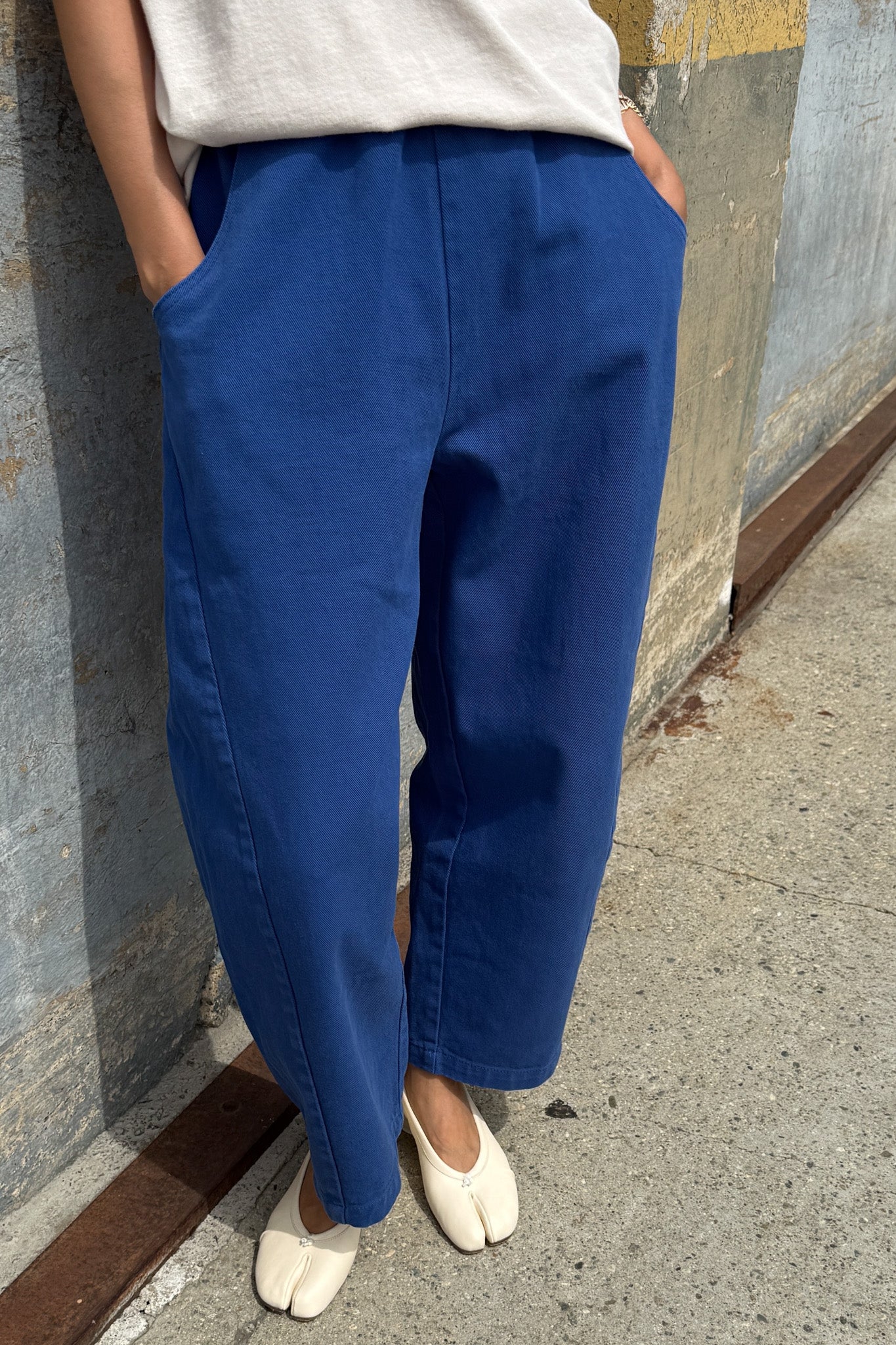Person wearing blue pants and white shoes standing against a wall.