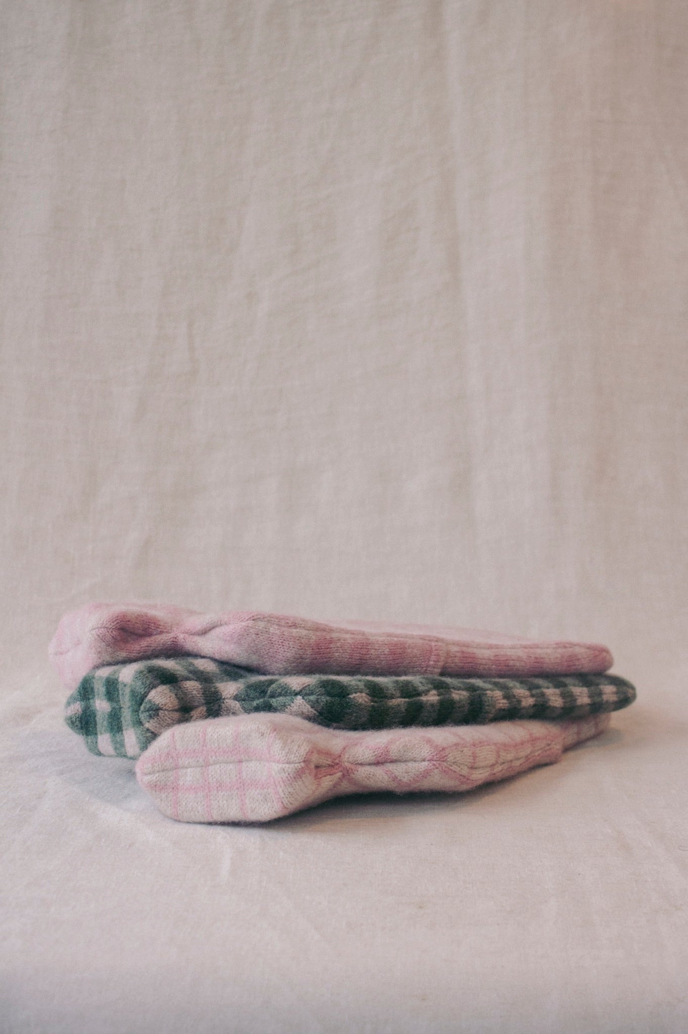 Stack of Chickpea hot water bottles with plaid and solid patterns on a neutral background
