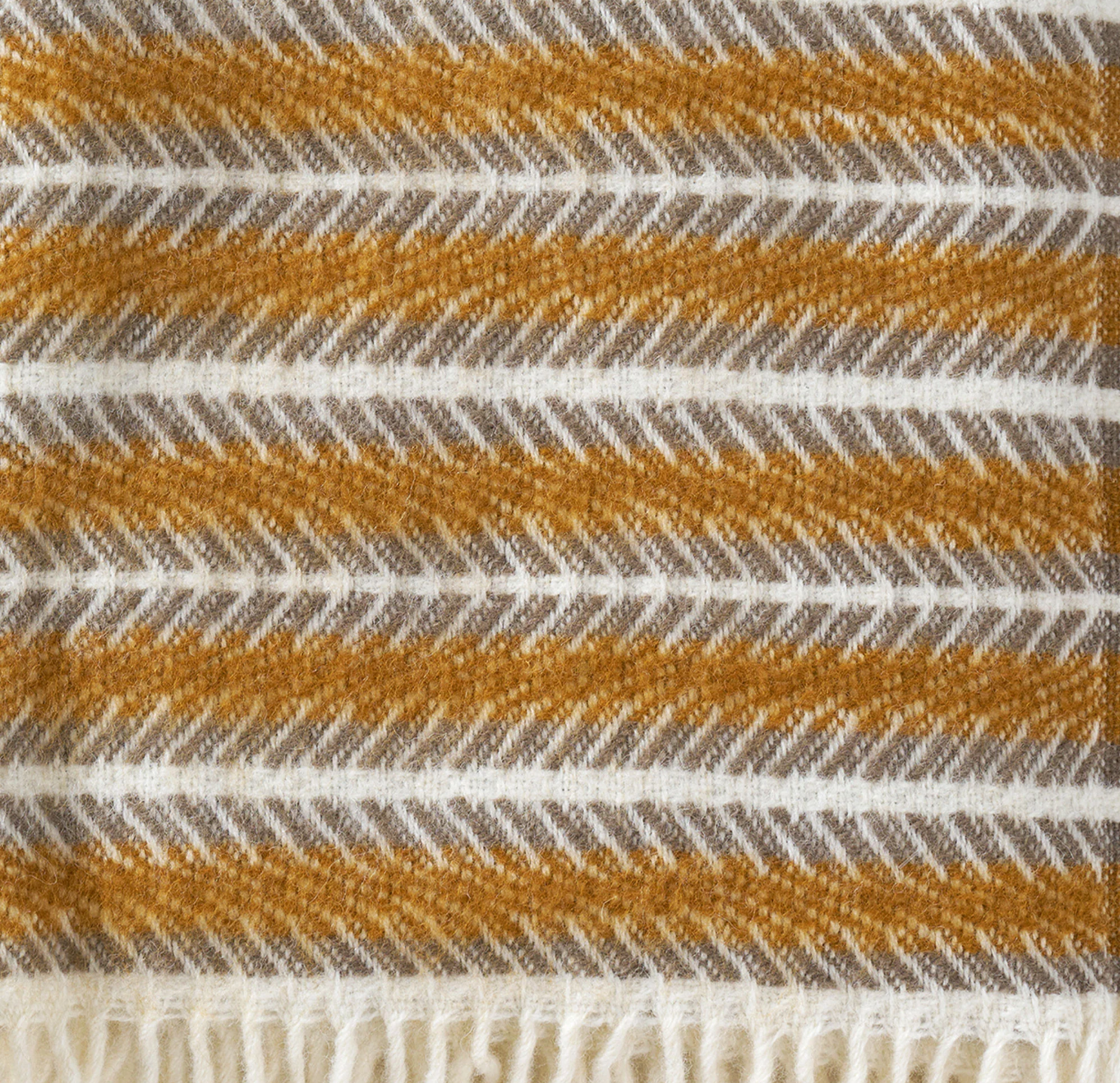 Soft lambswool blanket with an abstract stripe design. Amber, cream and grey colours. Finished with a tassel trim