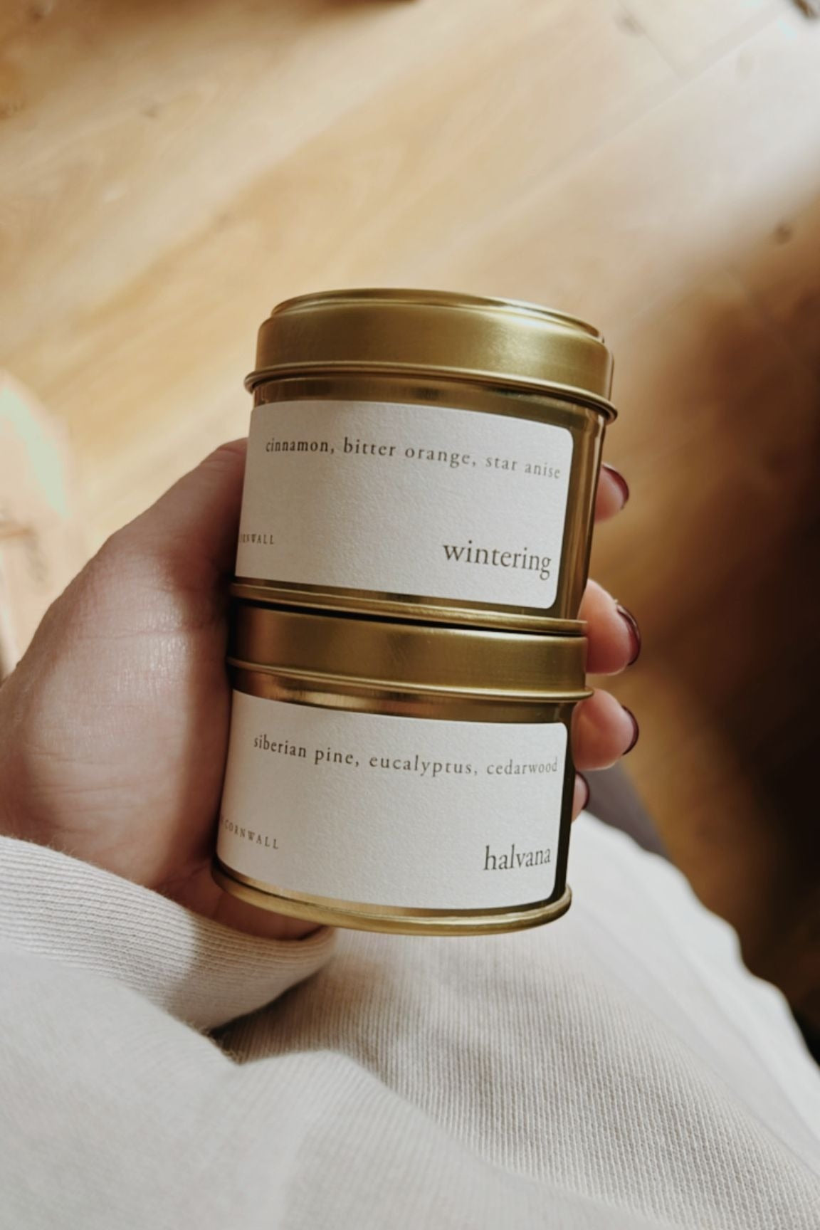 Hand holding a gold and white candle labeled 'wintering' with a blurred background