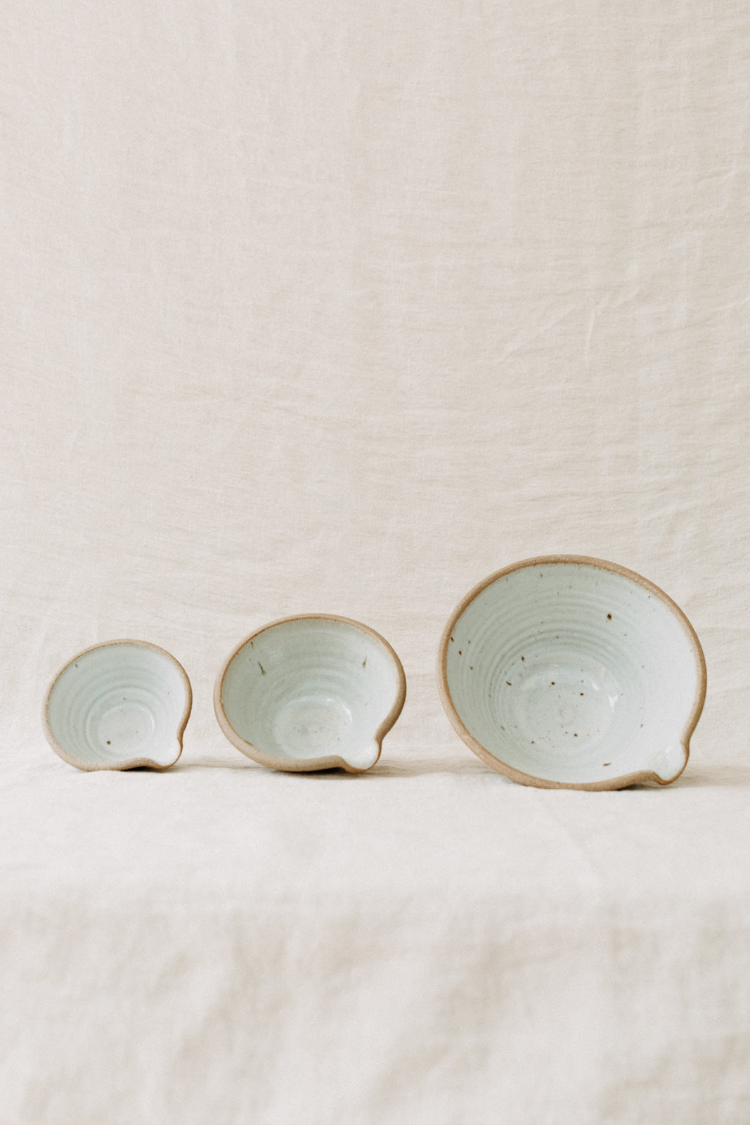 Handmade by the Leach Pottery Studio in St Ives. A set of three mixing bowls each finished with a lip for pouring. These bowls are glazed on the inside with a very pale duck egg blue dolomite glaze. The outside is unglazed for a natural and organic feel. Displayed so the inside is visible small on the left to large on the right.