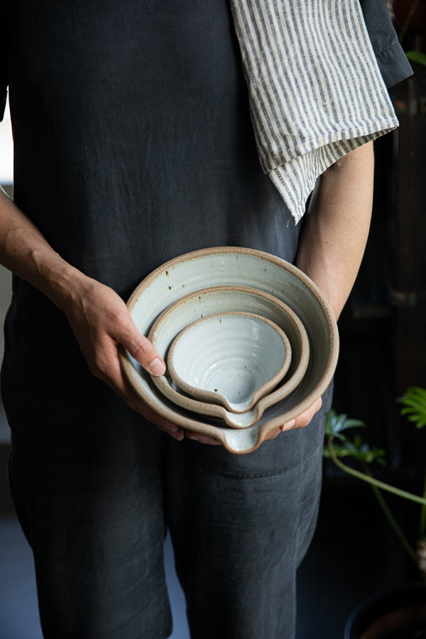 Handmade by the Leach Pottery Studio in St Ives. A set of three mixing bowls each finished with a lip for pouring. These bowls are glazed on the inside with a very pale duck egg blue dolomite glaze. The outside is unglazed for a natural and organic feel. Pictured being held in someones hands