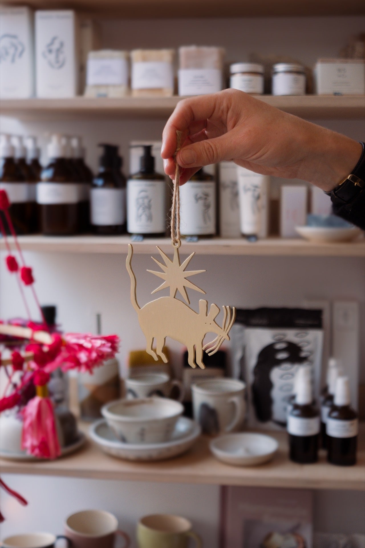 Hand holding a gold rmouse ornament with a shelf of products in the background