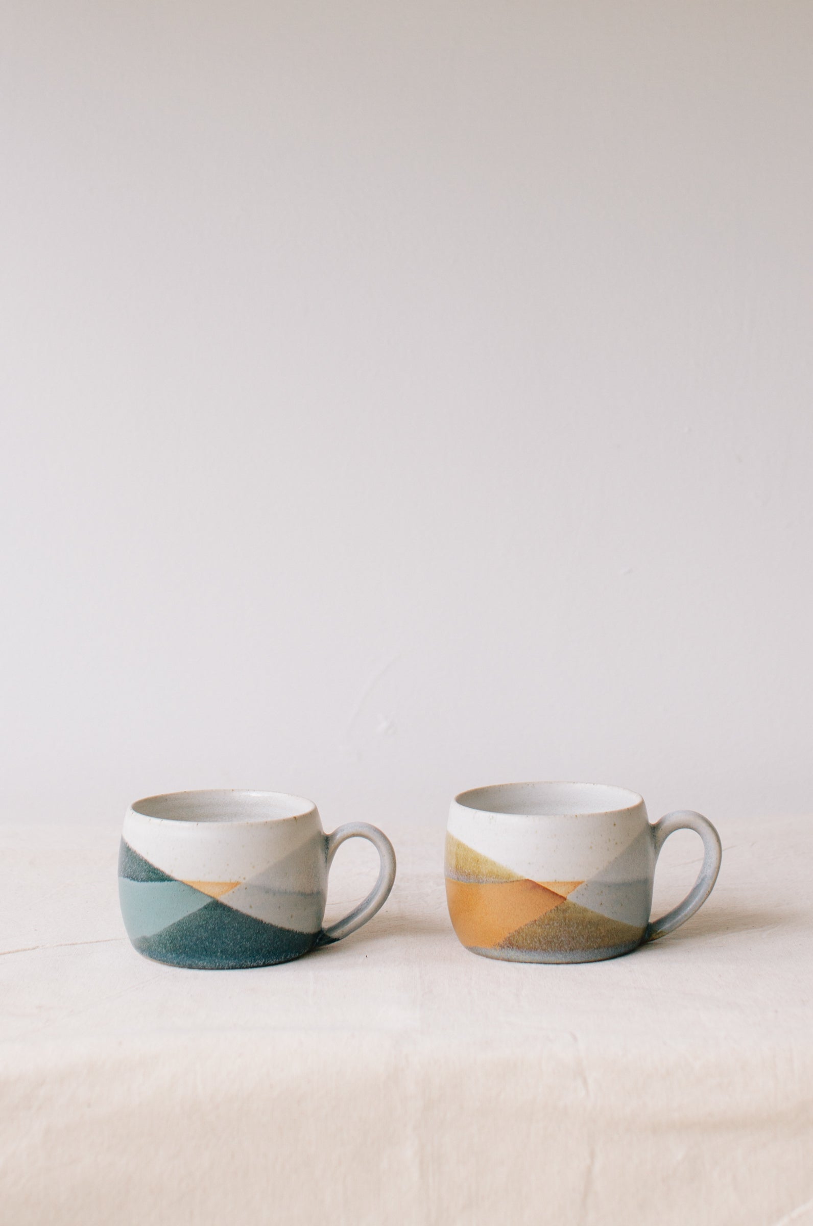 Handmade ceramic mug by Liz Vidal. Liz uses different tones of rust and brown glaze to dip her mug to create an abstract landscape design. Pictured here side by side