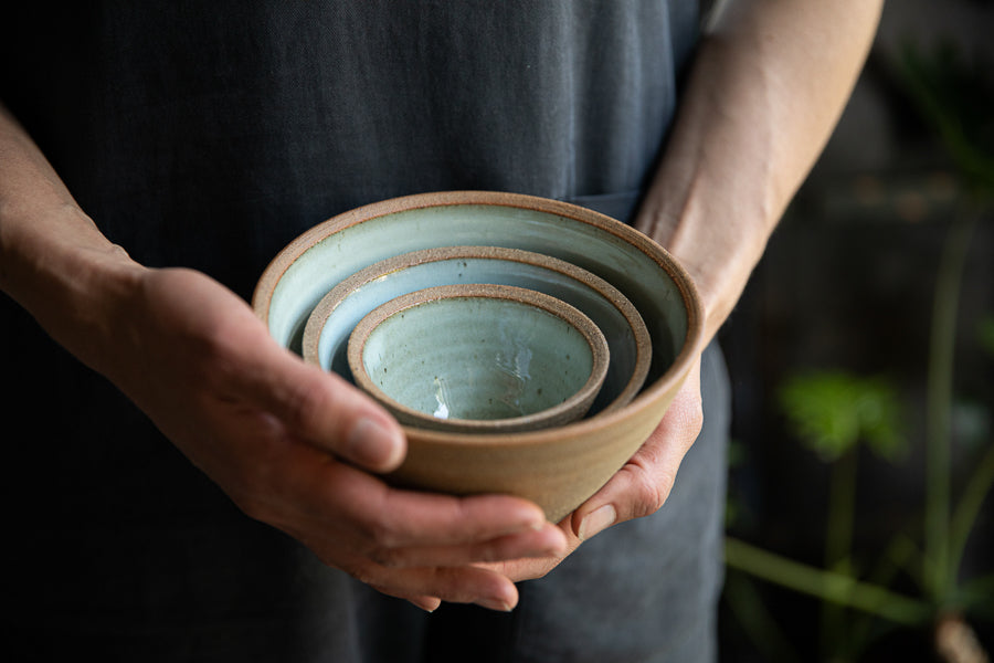 Handmade by the Leach Pottery Studio in St Ives. A set of three prepping bowls each one is glazed on the inside with a duck egg blue dolomite glaze. The outside is unglazed for a natural and organic feel. This images shows them being held as a stack.