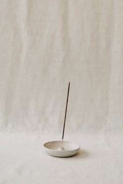 Handmade ceramic incense holder by Liz Vidal. This incense holder is a simple round shape and is finished with a hole for the incense to stand in. Liz has used a plain white glaze which shows small specs from the clay though it, giving it a beautiful natural finish.