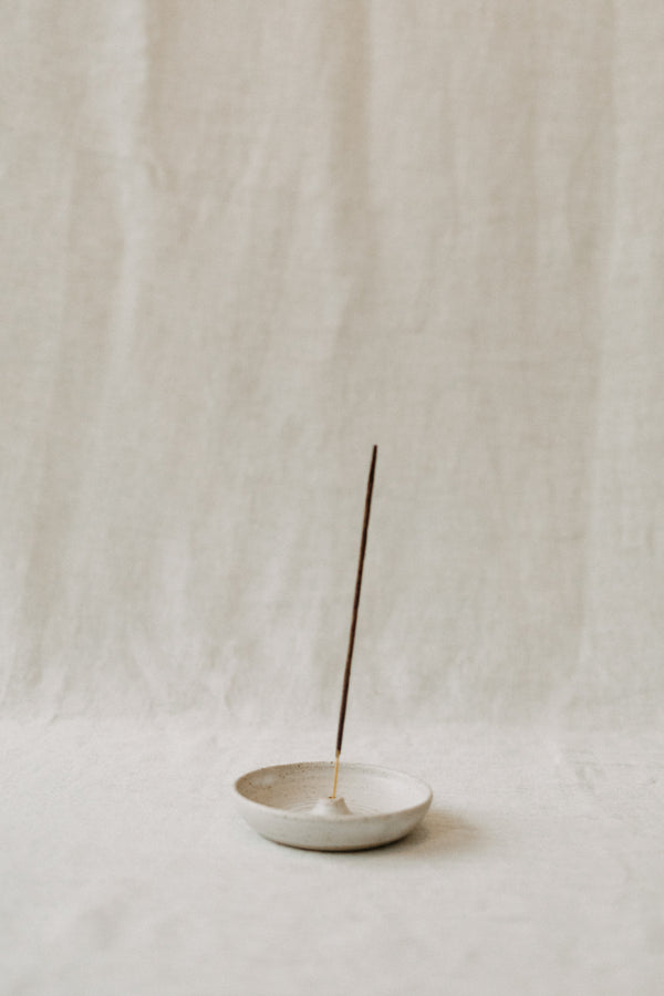 Handmade ceramic incense holder by Liz Vidal. This incense holder is a simple round shape and is finished with a hole for the incense to stand in. Liz has used a plain white glaze which shows small specs from the clay though it, giving it a beautiful natural finish.