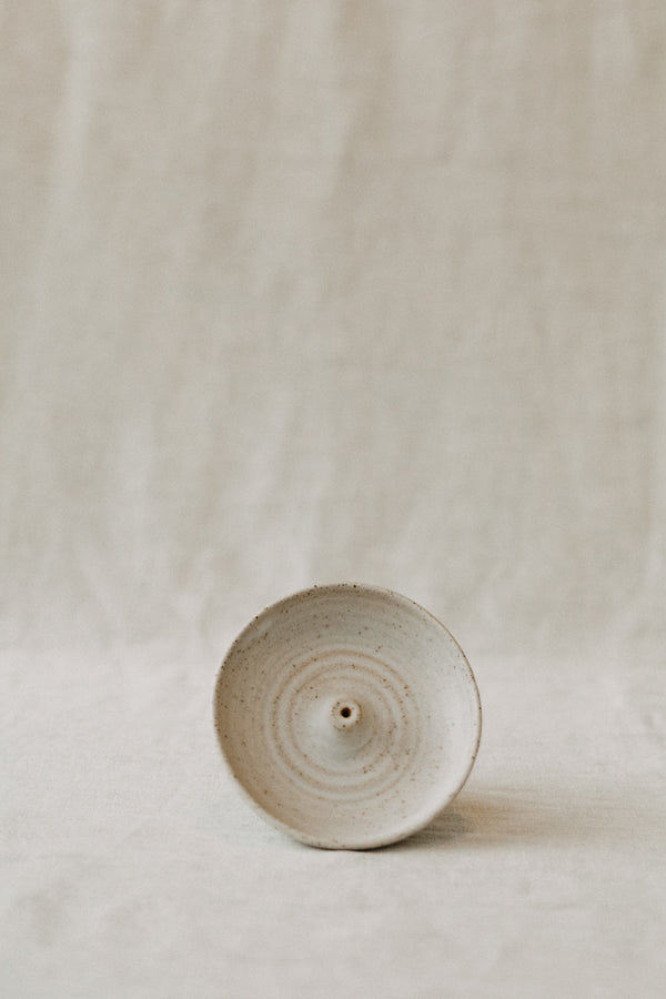 Handmade ceramic incense holder by Liz Vidal. This incense holder is a simple round shape and is finished with a hole for the incense to stand in. Liz has used a plain white glaze which shows small specs from the clay though it, giving it a beautiful natural finish.