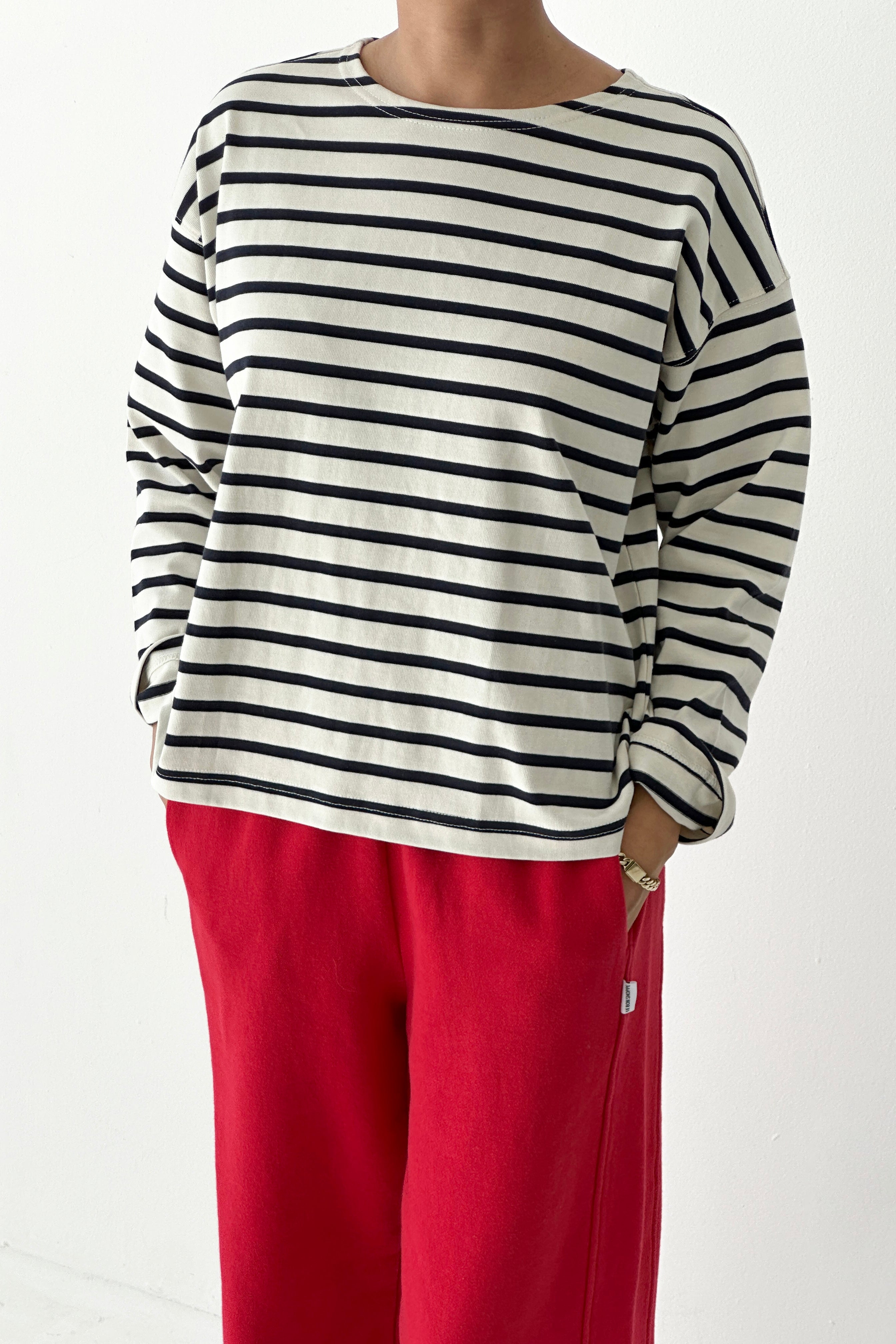 Person wearing a black and white striped long-sleeve shirt with red pants on a white background