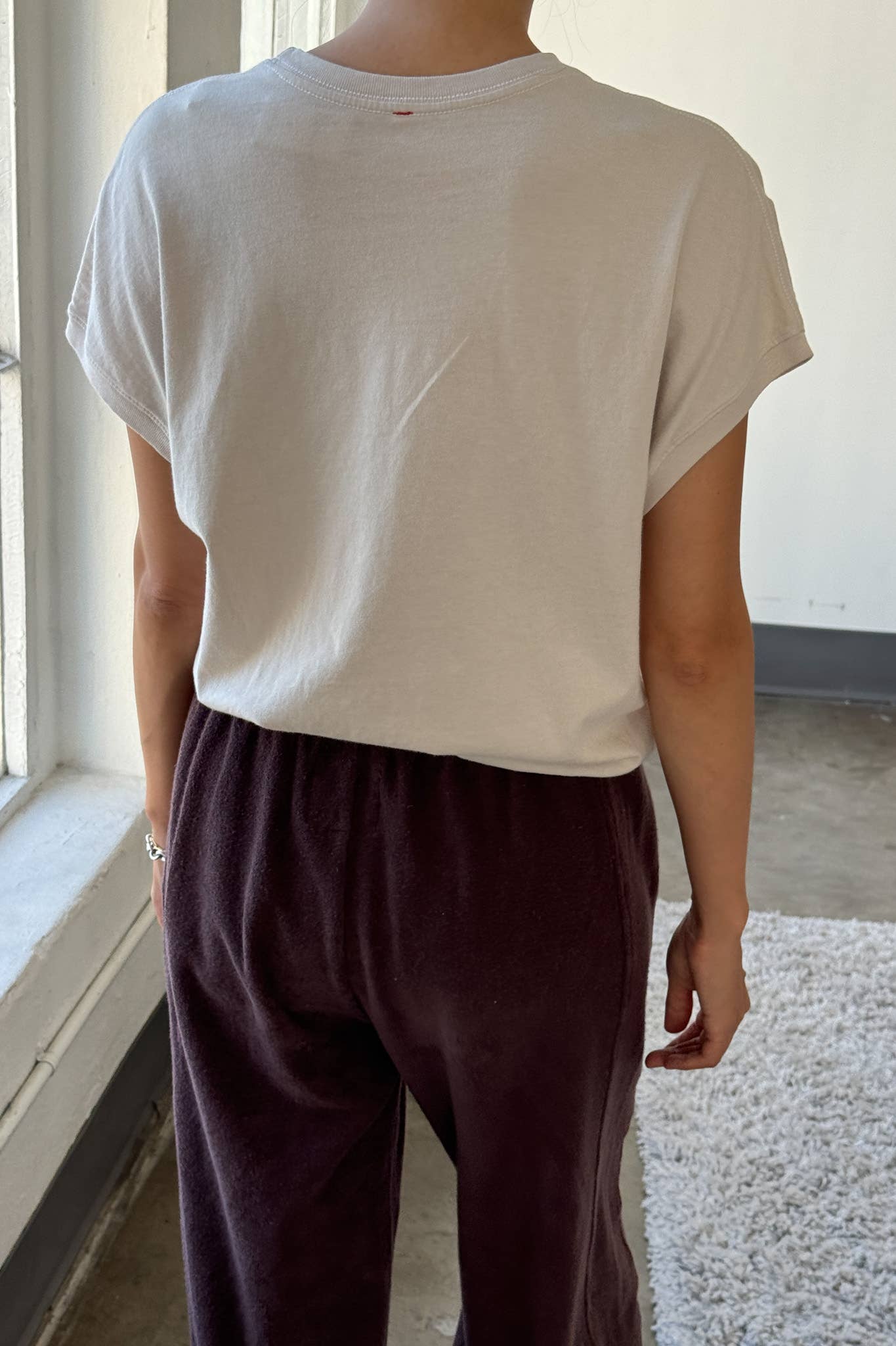 Person wearing a white t-shirt and dark pants in a minimal indoor setting
