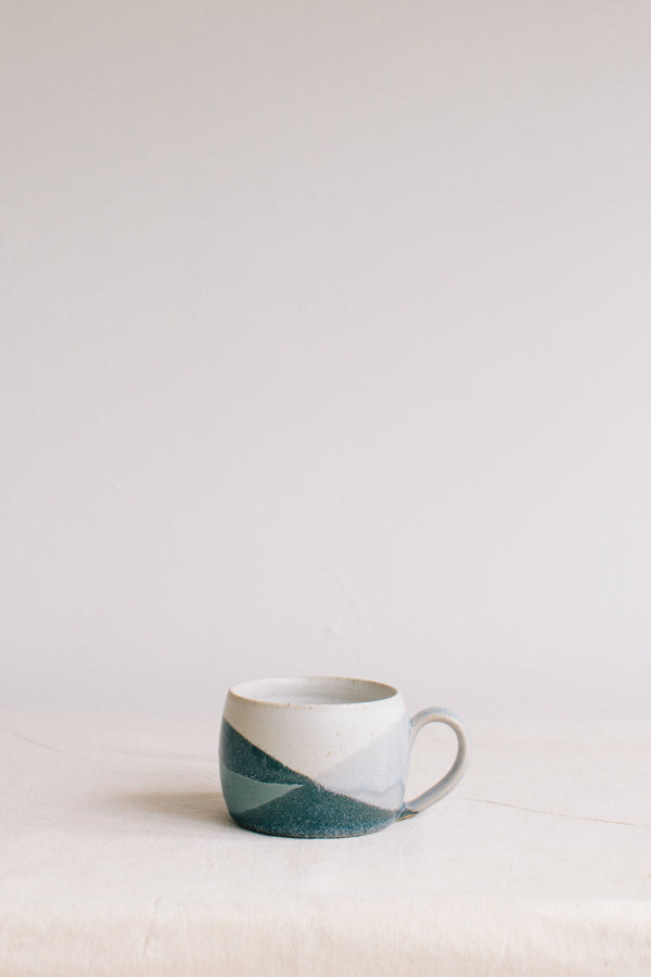 Handmade ceramic mug by Liz Vidal. Liz uses different tones of blue glaze to dip her mug to create an abstract landscape design.