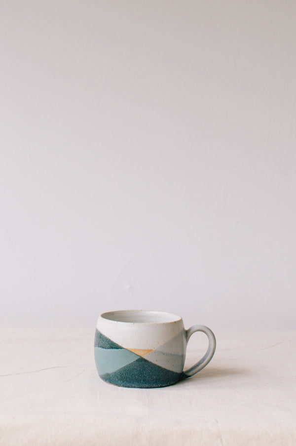 Handmade ceramic mug by Liz Vidal. Liz uses different tones of blue glaze to dip her mug to create an abstract landscape design.