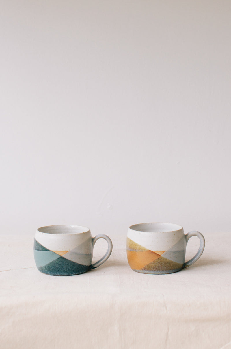 Handmade ceramic mug by Liz Vidal. Liz uses different tones of blue glaze to dip her mug to create an abstract landscape design.