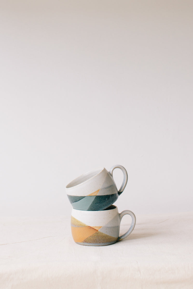 Handmade ceramic mug by Liz Vidal. Liz uses different tones of blue glaze to dip her mug to create an abstract landscape design.