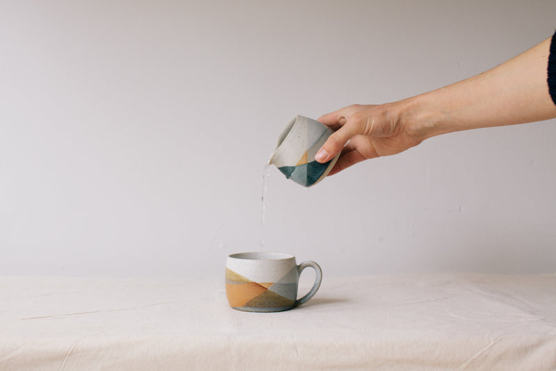 Handmade ceramic jug by Liz Vidal. Liz uses different tones of blue glaze to dip her jugs to create an abstract landscape design. Pictured here pouring from the jug into the abstract mug.
