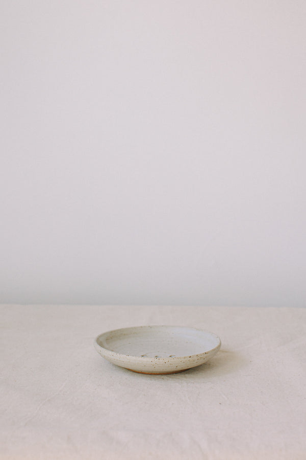 Handmade ceramic soap dish by Liz Vidal. This incense holder is a simple round shape and is finished with 3 holes and a small foot plate to allow the soap to drain. Liz has used a plain white glaze which shows small specs from the clay though it, giving it a beautiful natural finish.