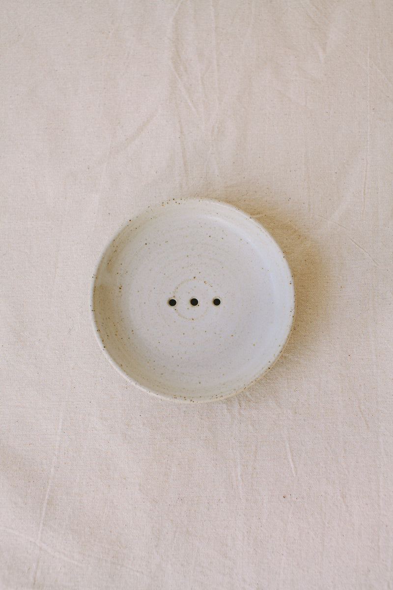 Handmade ceramic soap dish by Liz Vidal. This incense holder is a simple round shape and is finished with 3 holes and a small foot plate to allow the soap to drain. Liz has used a plain white glaze which shows small specs from the clay though it, giving it a beautiful natural finish.